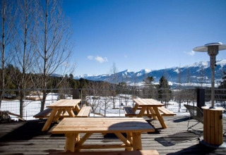 Wooden picnic tables on a terrace with stunning snowy mountain views at Les Chalets Huttopia de Font-Romeu.