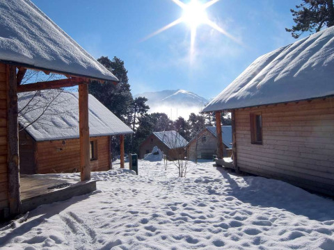 Sonnige, schneebedeckte Holzchalets im Winter am Les Chalets Huttopia de Font-Romeu, Occitanie, Frankreich.