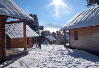 Sonnige, schneebedeckte Holzchalets im Winter am Les Chalets Huttopia de Font-Romeu, Occitanie, Frankreich.