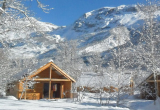 Chalets en bois sous la neige avec montagnes enneigées aux Chalets Huttopia de Vallouise, Provence, France.