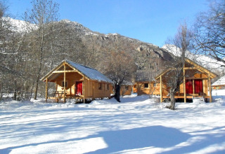 Wooden cabins at Les Chalets Huttopia de Vallouise, surrounded by snowy landscape and mountains in France.