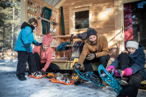 Gezin doet sneeuwschoenen aan voor een chalet bij Les Chalets Huttopia de Vallouise, Provence-Alpes-Côte d’Azur, Frankrijk.