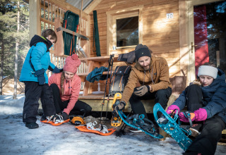 Family putting on snowshoes outside a cabin at Les Chalets Huttopia de Vallouise in Provence-Alpes-Côte d’Azur, France.