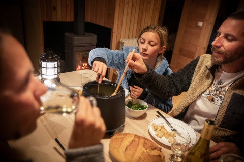 Gezin eet fondue in een knus houten chalet bij Les Chalets Huttopia de Vallouise in Frankrijk.