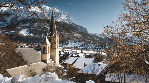 Pueblo nevado de Vallouise, Francia, con una iglesia y montañas al fondo durante el invierno.