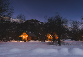 Chalets chaleureux éclairés dans la neige au crépuscule à Huttopia de Vallouise en Provence-Alpes-Côte d’Azur.