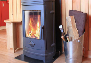 Poêle à bois allumé dans un chalet chaleureux, à côté d’un seau en métal rempli de bûches et d’accessoires.