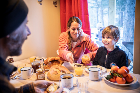 Familia disfrutando el desayuno junta en una mesa en Les Chalets Huttopia de Vallouise, Provenza-Alpes-Costa Azul, Francia.