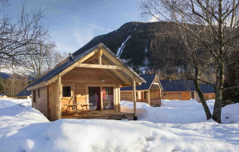 Cabañas de madera en Les Chalets Huttopia de Vallouise, Provenza-Alpes-Costa Azul, rodeadas de nieve y montañas.