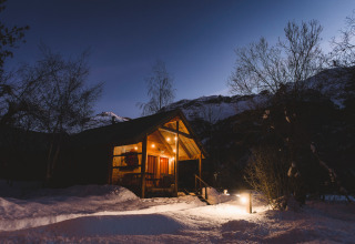 Gemütliche Berghütte bei Nacht, beleuchtet im Schnee, Les Chalets Huttopia de Vallouise, Alpen, Frankreich.