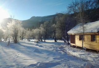 Cabaña de madera junto a paisaje nevado y árboles helados bajo el sol en Vallouise, Provenza-Alpes, Francia.