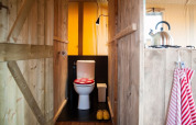 Interiør af safari telt med klimaanlæg, viser et trætoiletområde og køkken med elkedel.