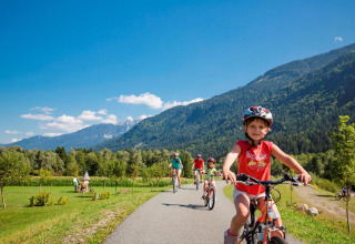 Bambini e adulti in bicicletta su un sentiero panoramico vicino a un glamping con montagne sullo sfondo.