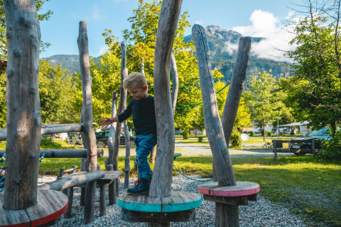 Ein Kind spielt auf einem naturbelassenen Spielplatz im Glamping-Bereich mit Bergen im Hintergrund.