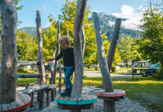 Un bambino gioca su un parco giochi in legno in un glamping con montagne sullo sfondo.