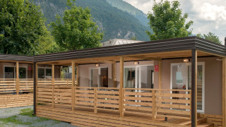 Cottage moderne doté d'une terrasse en bois, entouré d'arbres, avec vue sur les montagnes en arrière-plan.