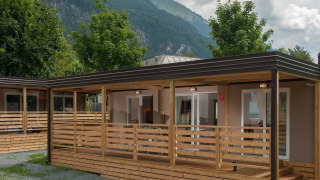 Cottage moderno con veranda in legno, circondato da alberi e montagne suggestive sullo sfondo.
