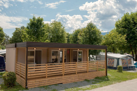 Modernes Cottage am Hermagor-Nassfeld in Österreich mit Holzterrasse und Bäumen unter blauem Himmel.