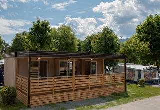 Modern huisje bij Hermagor-Nassfeld in Oostenrijk met houten terras, omringd door groene bomen en blauwe lucht.
