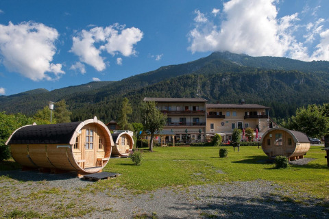 Tractor cabin: Cabañas de madera en forma de barril frente a un lodge acogedor con montañas detrás.