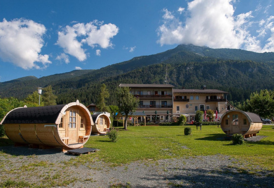 Tractor cabin: Casette di legno a forma di botte davanti a un lodge, con montagne sullo sfondo verde.
