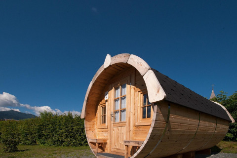 Cabaña de madera en forma de barril en Tractor cabin lodge, Hermagor-Nassfeld, Austria, bajo cielo azul claro.