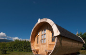 Træhytte i tøndeform ved Tractor cabin lodge, Hermagor-Nassfeld, Østrig, under en klar blå himmel.