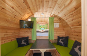 Interiør af en hyggelig træhytte med grønne gardiner, siddepladser, bord og tv i Tractor cabin i Hermagor-Nassfeld, Østrig.