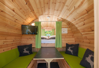 Interno in legno della lodge Tractor Cabin a Hermagor-Nassfeld, Austria, con panche verdi, tavolo e TV.