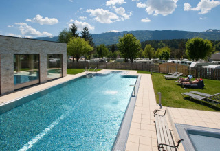 Piscina all'aperto presso una struttura glamping, montagne sullo sfondo e ospiti che prendono il sole sul prato.
