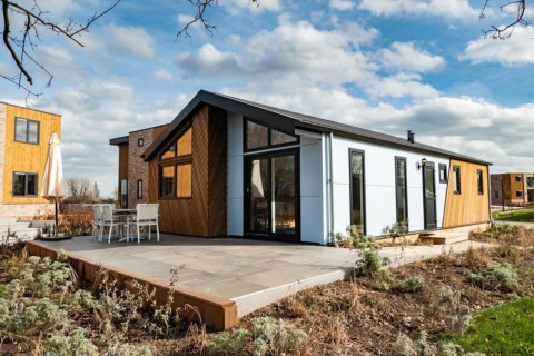 Moderne Hackfort lodge met grote ramen en terras, omgeven door groen en soortgelijke lodges in de buurt.