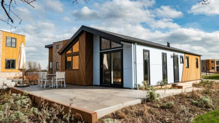 Moderne Hackfort lodge met grote ramen en terras, omgeven door groen en soortgelijke lodges in de buurt.