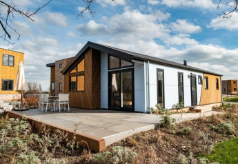 Moderne Hackfort lodge met grote ramen en terras, omgeven door groen en soortgelijke lodges in de buurt.