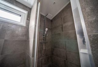 Ducha moderna con azulejos grises y ventana en Hackfort Lodge de Vakantiepark Aan de Maas, Países Bajos.