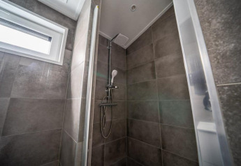 Modern shower with gray tiles and window inside Hackfort Lodge at Vakantiepark Aan de Maas, Netherlands.