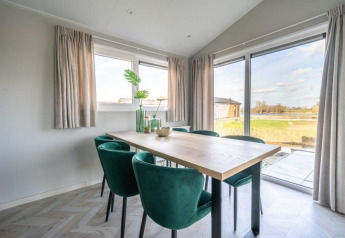 Sala da pranzo luminosa nella lodge Hackfort a Vakantiepark Aan de Maas, Paesi Bassi, con sedie verdi.