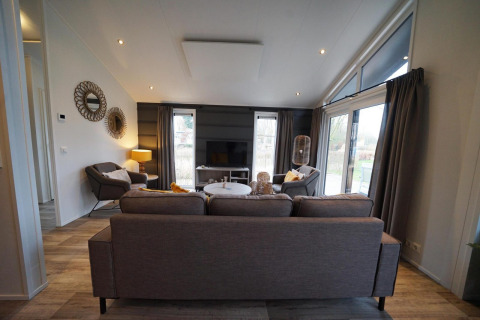 Moderne woonkamer in lodge Hackfort op Vakantiepark Aan de Maas, Nederland, met bank en grote ramen.