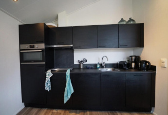 Moderne schwarze Küche in einer Lodge im Vakantiepark Aan de Maas, Niederlande, mit Geräten und Holzfußboden.
