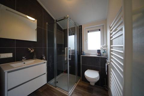 Moderne badkamer bij Hackfort-lodge op Vakantiepark Aan de Maas met glazen douche en hangend toilet.