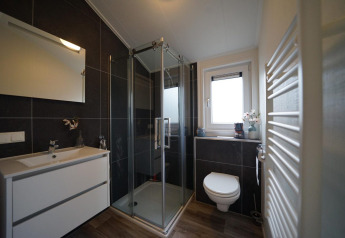 Moderne badkamer bij Hackfort-lodge op Vakantiepark Aan de Maas met glazen douche en hangend toilet.