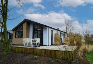Lodge Hackfort op Vakantiepark Aan de Maas in Nederland, met houten terras en tuinmeubelen onder blauwe lucht.