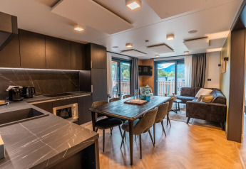 Zona moderna de sala y cocina en el lodge Wulfenia, con vistas a las montañas por ventanas grandes.