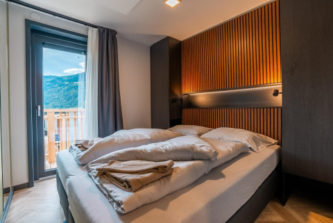 Moderne slaapkamer in Wulfenia lodge bij de Ossiacher See in Oostenrijk, met balkon en uitzicht op bergen.