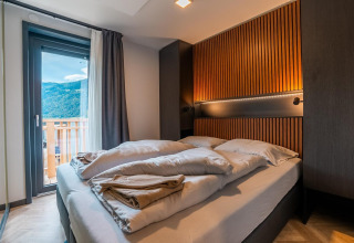 Moderne slaapkamer in Wulfenia lodge bij de Ossiacher See in Oostenrijk, met balkon en uitzicht op bergen.