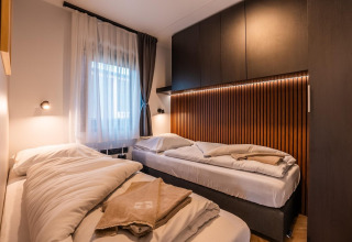 Moderne tweepersoonskamer met houten wand, zachte verlichting en bedden bij Wulfenia aan de Ossiacher See, Oostenrijk.