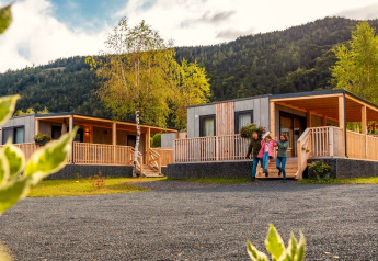 Familie vor der Seerose-Lodge mit modernen Holzhäusern inmitten grüner Berge und schöner Natur.