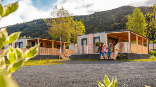 Family standing outside Seerose lodge, featuring modern wooden cabins and a mountainous wooded landscape.
