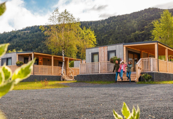 Familia afuera de la cabaña Seerose con alojamientos modernos de madera en un hermoso entorno montañoso.