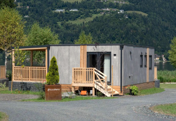 Lodge Enzian by the lake, featuring a modern wood exterior, terrace, greenery, and scenic mountains.