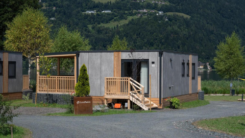Lodge Enzian aan een meer, met moderne houten gevel, terras, veel groen en bergen rondom.